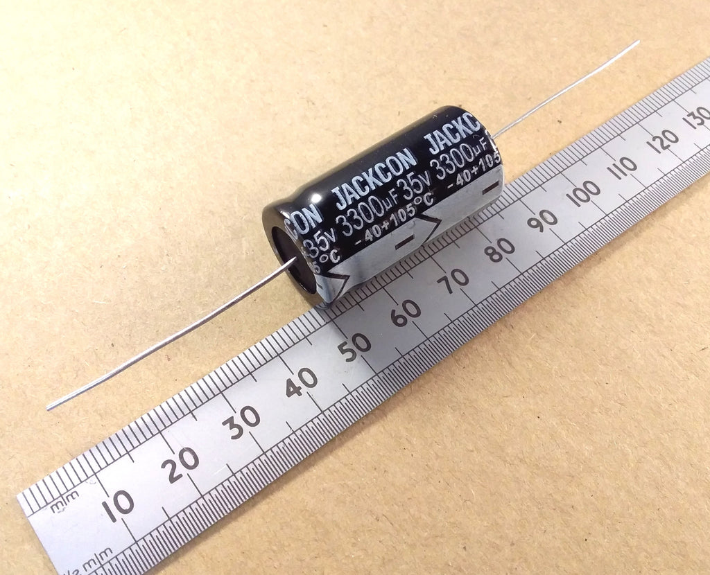 A black cylindrical axial electrolytic capacitor with silver leads, labeled 'JACKSON 35V 3300uF -40C 105C', shown next to a metal ruler on a beige background.