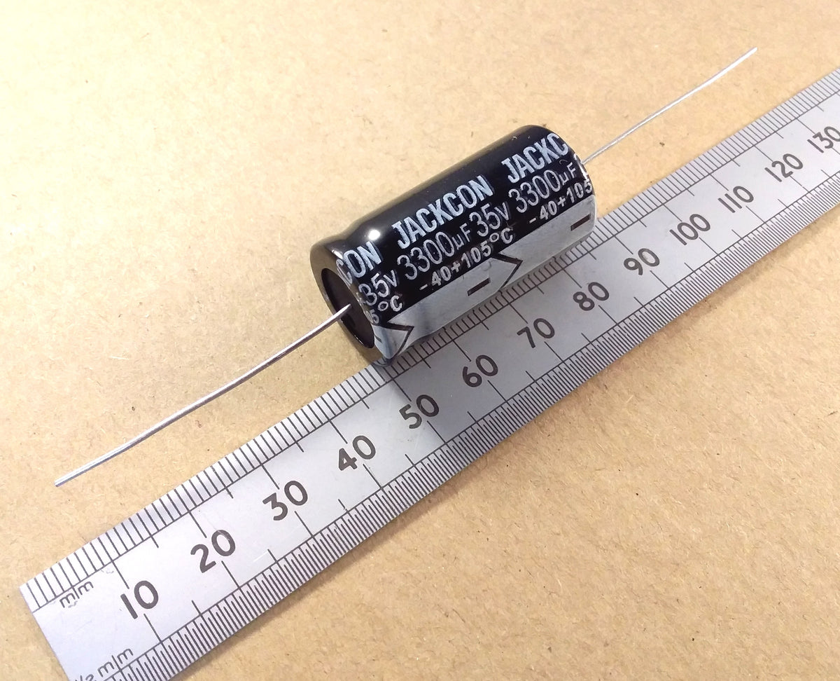 A black cylindrical axial electrolytic capacitor with silver leads, labeled 'JACKSON 35V 3300uF -40C 105C', shown next to a metal ruler on a beige background.