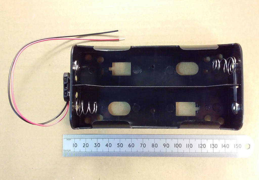 HJW electronics black plastic 4 X D cell battery holder with attached red, black, and white wires, shown next to a metal ruler on a beige background with PP3 connector clip.